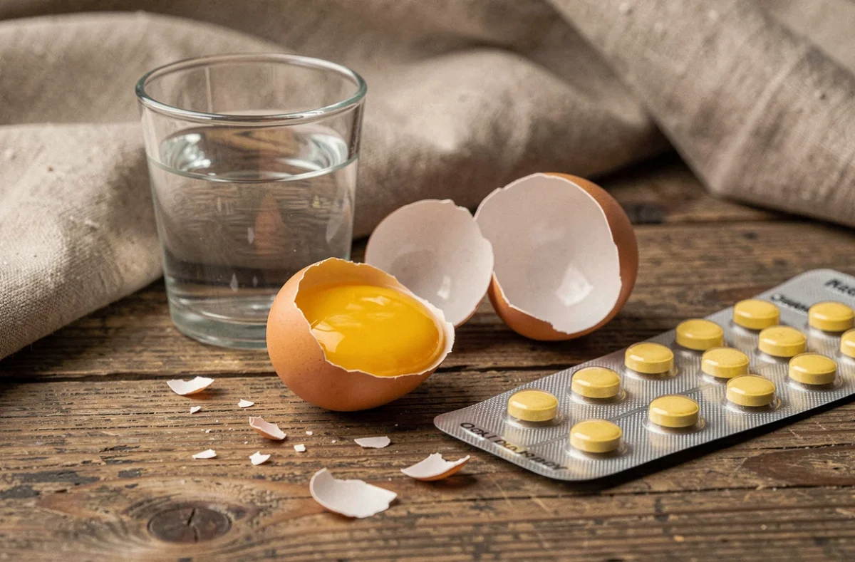 Gros plan sur un œuf cassé et des comprimés digestifs sur une table en bois, symbolisant les problèmes de digestion et les rots nauséabonds